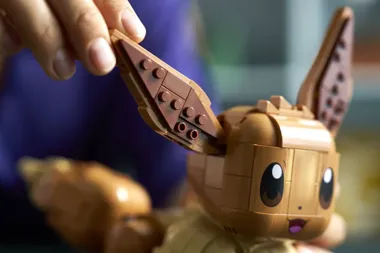 Dłoń ustawia klockową figurkę Eevee z uniesionym uchem.