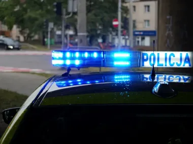 Zbliżenie na włączony niebieski sygnał świetlny na dachu policyjnego radiowozu oznaczonego napisem POLICJA, stojącego przy ulicy w mieście.