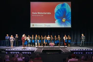 Uczestnicy gali wręczenia nagród Pomorski Bratek 2026 stoją na scenie z kwiatami i niebieskimi torbami podczas Gali Wolontariatu w województwie pomorskim.